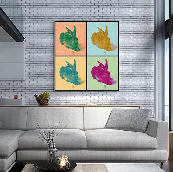 Ein modernes Wohnzimmer mit einem großen Pop-Art-Wandbild an einer weißen Ziegelwand. Das Kunstwerk zeigt vier farbintensive Darstellungen des Dürer Hasen in den Farben Grün, Blau, Gelb und Magenta. Die Einrichtung des Raumes ist minimalistisch mit einem hellgrauen Sofa und großen Fenstern, die viel natürliches Licht hineinlassen.