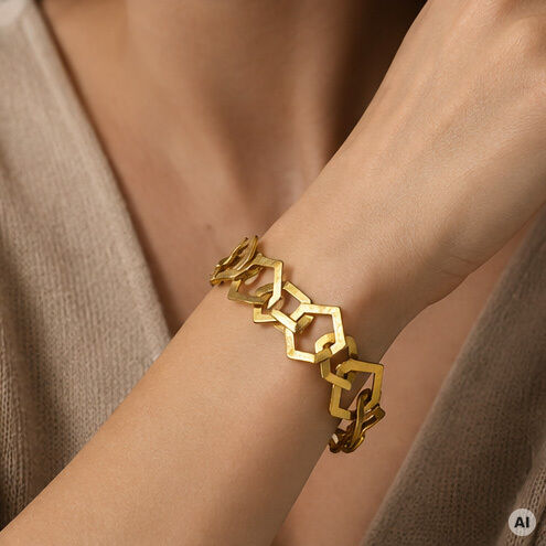 Nahaufnahme eines goldfarbenen Armbands von Ars mundi aus 22 Karat vergoldetem Messing am Handgelenk einer Frau. Das Armband besteht aus geometrisch verschlungenen, offenen Vierecken und wirkt hochwertig verarbeitet. Im Hintergrund ist ein beiger Stoff zu sehen.