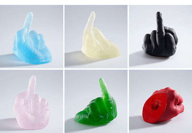 Eine künstlerische Glasinstallation von Ai Weiwei, die mehrere Handgesten zeigt, in verschiedenen Farben wie Blau, Weiß, Schwarz, Rosa, Grün und Rot. Die Hände sind in einer stilisierten 'Mittelfinger' Geste geformt.