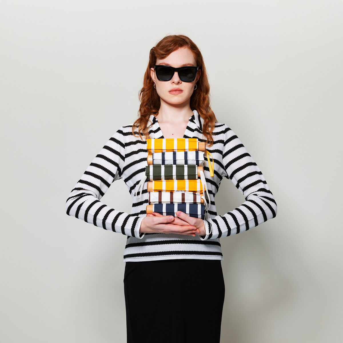 Eine Frau trägt einen gestreiften Taschenschirm in Navy und Weiß. Sie trägt eine Sonnenbrille, einen gestreiften Pullover und hält den Schirm vor sich.
