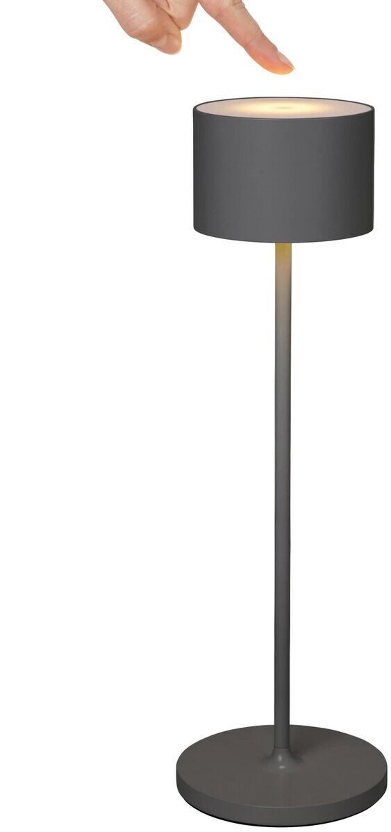 Mobile LED-Tischleuchte »FAROL« in schwarzer Farbe. Eine Hand berührt die Oberseite der Leuchte, die auf einem langen, schlanken Standfuß ruht und ein warmes gelbes Licht ausstrahlt.