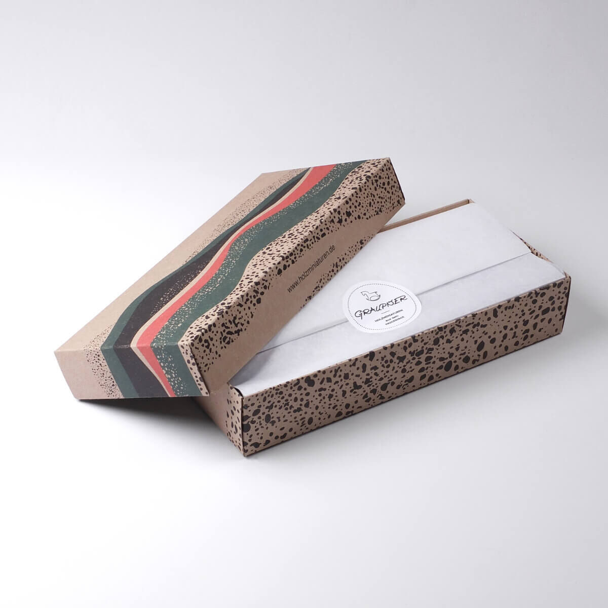 Eine Geschenkbox, die drei handgefertigte Weihnachtsmänner als Baumschmuck enthält. Die Box hat ein dekoratives Design in Brauntönen mit grünen und roten Akzenten.