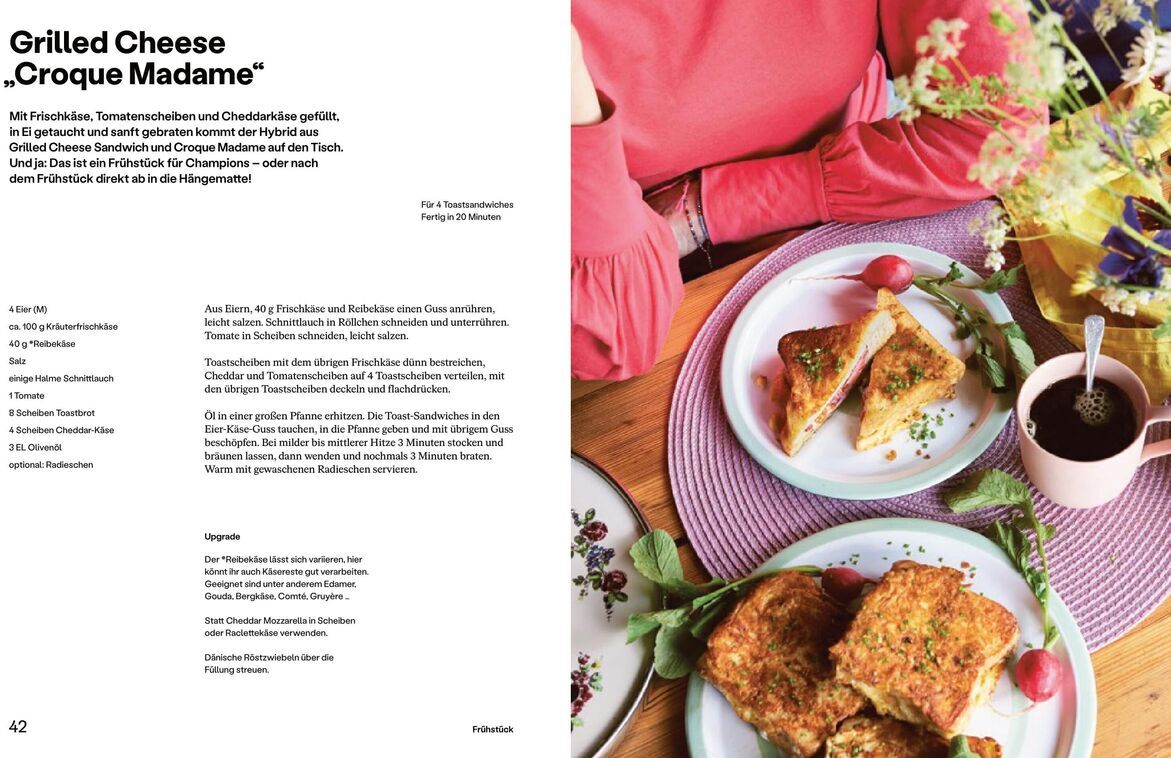 Eine Seite aus dem Buch 'Einfach Urlaub' von Paul Stevan zeigt ein Rezept für Grilled Cheese 'Croque Madame'. Ein Teller mit zwei Grilled Cheese Sandwiches, dekoriert mit Tomaten und einem Schnittlauchbündel, steht auf einem weißen Tisch. Daneben sind bunte Blumen und weitere Frühstücksutensilien dekorativ platziert.