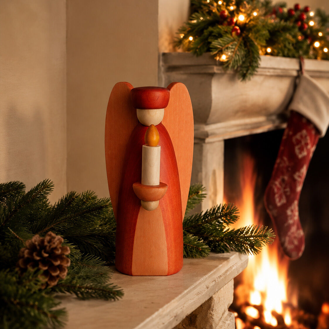 Handgefertigte Holzfigur »Lichterengel« von Björn Köhler steht auf einem Kaminsims, umgeben von Tannenzweigen, Zapfen und weihnachtlicher Deko. Im Hintergrund brennt ein Kaminfeuer und ein Strumpf hängt am Kamin. Die Figur ist rot-orange lasiert, Maserung sichtbar.