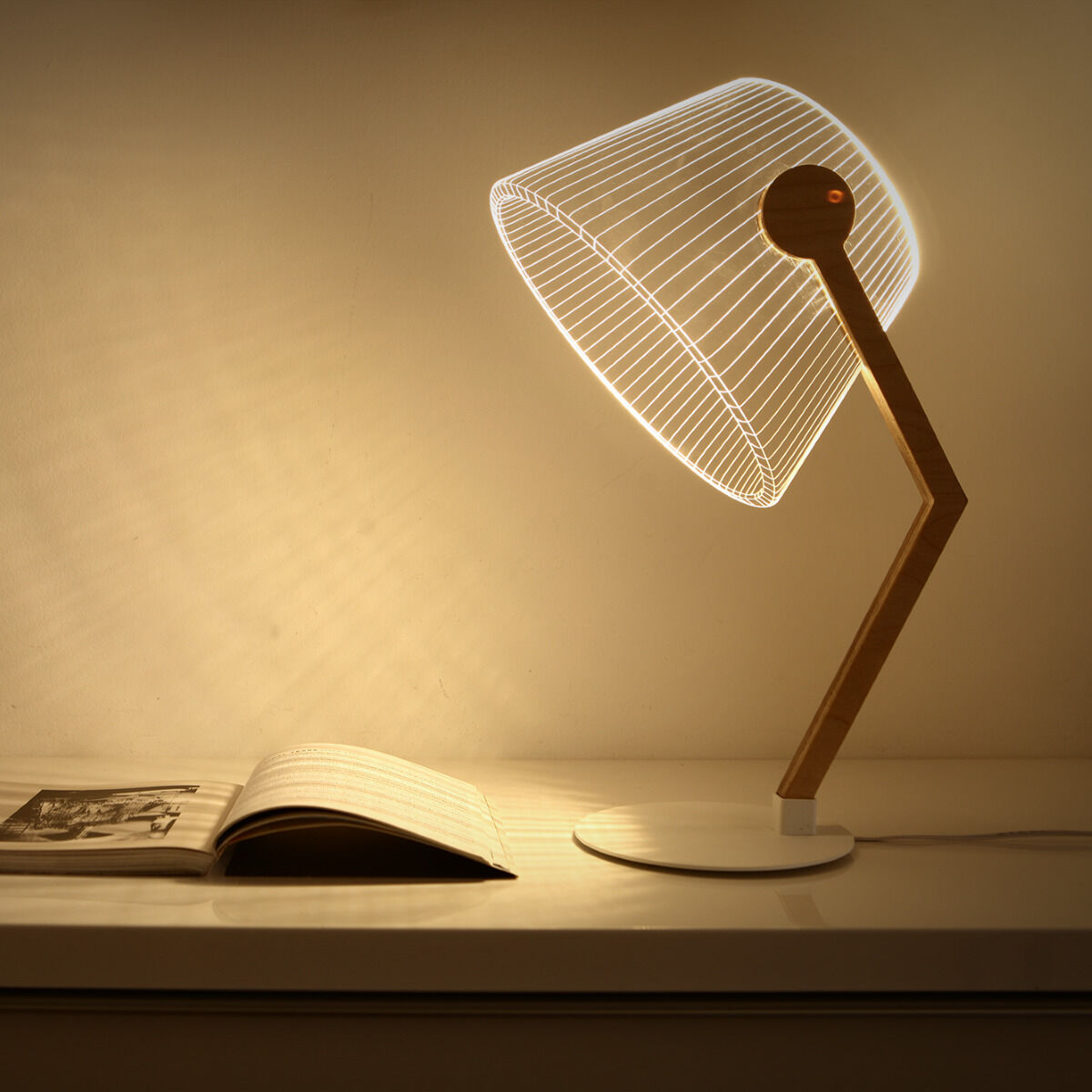 Eine moderne 3D-Lampe namens ZIGGi in Holzoptik steht auf einem weißen Tisch. Die Lampe hat ein minimalistisches Design, das aus einer Holzbasis und einem Acrylglas-Schirm besteht, der in weißem Licht erstrahlt. Daneben liegt ein geöffnetes Buch.
