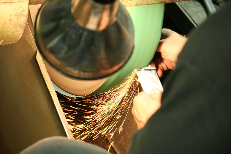 Ein Mann oder eine Frau schärft ein chinesisches Kochmesser Chai Dao an einem Schleifstein, während Funken sprühen.