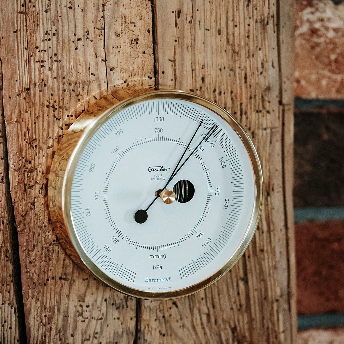 Ein weißes Barometer mit goldfarbenem Metallrahmen und schwarzen Zahlen, das auf einem rustikalen Holzhintergrund montiert ist. Es trägt den Schriftzug »ZEIT-Sonderedition POLAR Barometer«.
