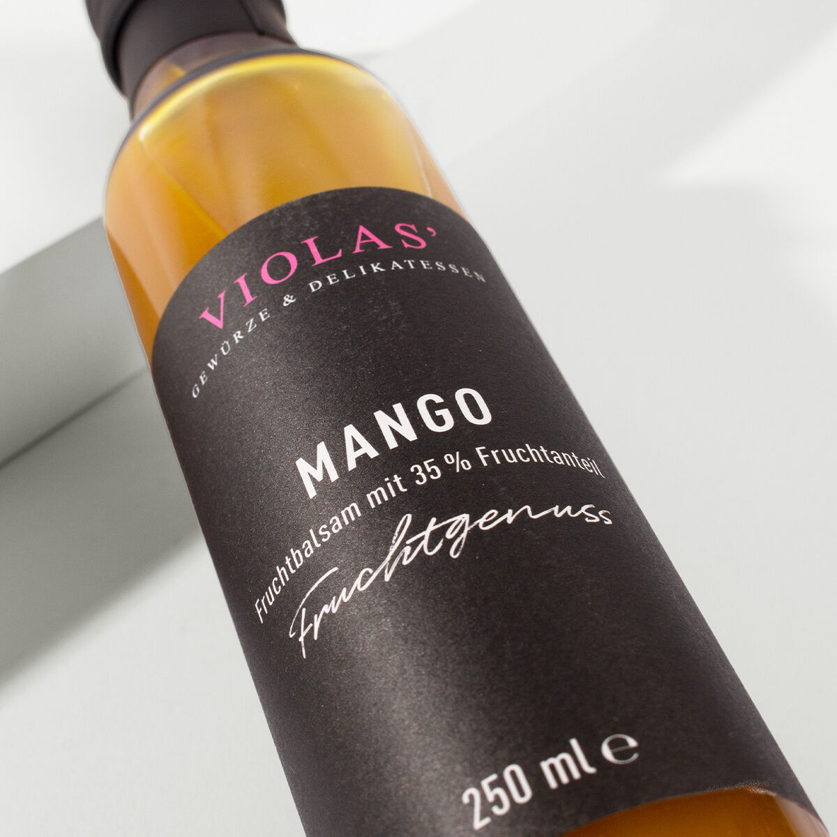 Eine 250-ml-Flasche Mangobalsam mit einem Etikett, das in Schwarz und Rosa gestaltet ist und von der Marke Violas stammt. Der Aufdruck besagt, dass der Balsam einen Fruchtgehalt von 35% hat.