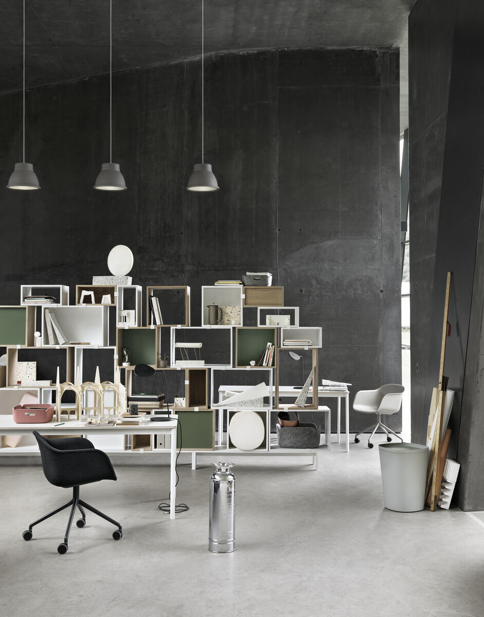 Ein modernes Büro mit einem stilvollen Aufbewahrungskorb »Restore« in einer skandinavisch inspirierten Einrichtung. Regale und Tische sind ordentlich angeordnet und bieten Platz für diverse Gegenstände. Dunkle Wände und minimalistische Dekoration prägen den Raum.