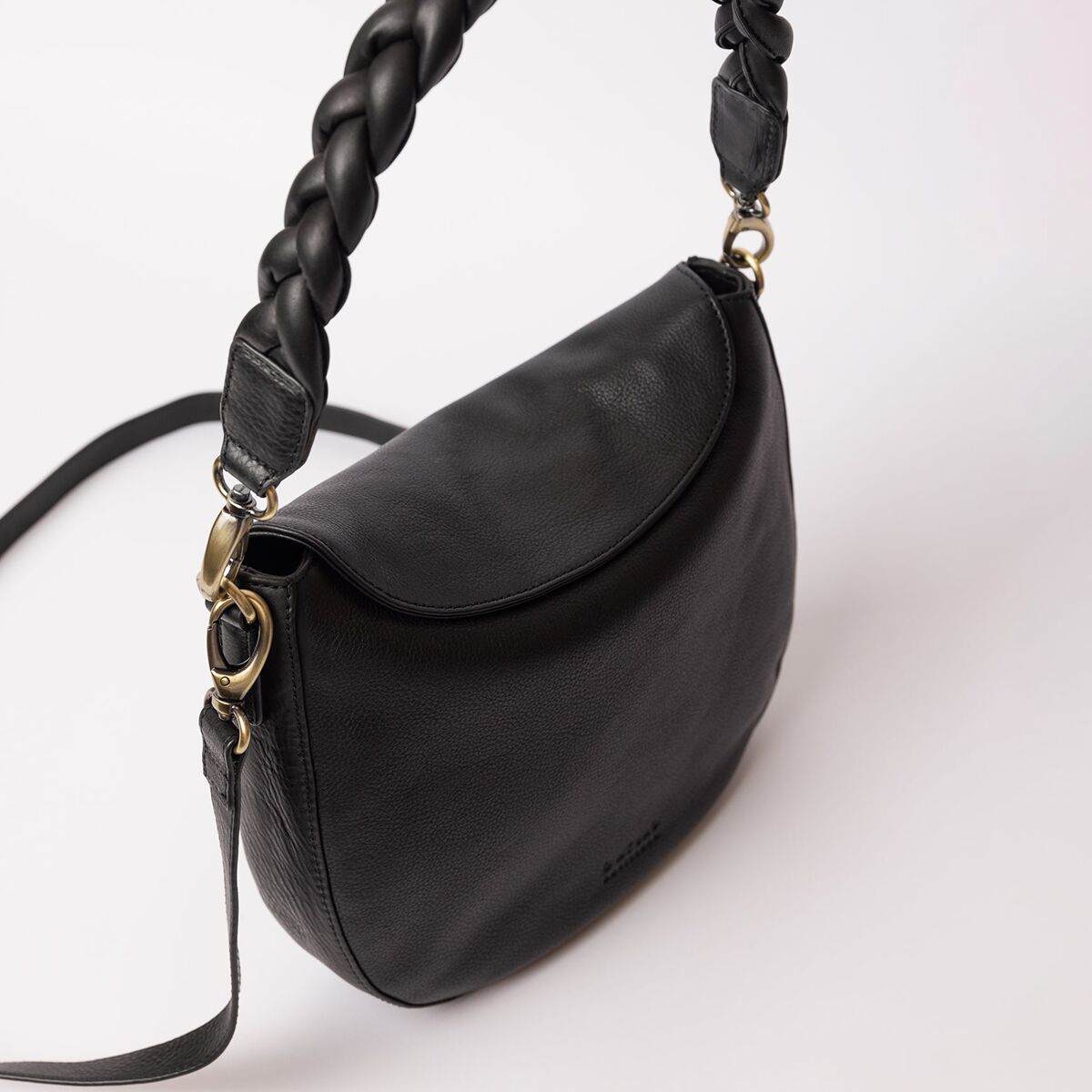 Die Abbildung zeigt eine elegante, schwarze Umhängetasche aus Lederimitat mit einem auffällig geflochtenen Henkel und goldfarbenen Metallelementen. Die Tasche hat eine abgerundete Klappe und ein schlichtes, modernes Design, das für den täglichen Gebrauch sowie zu besonderen Anlässen geeignet ist.