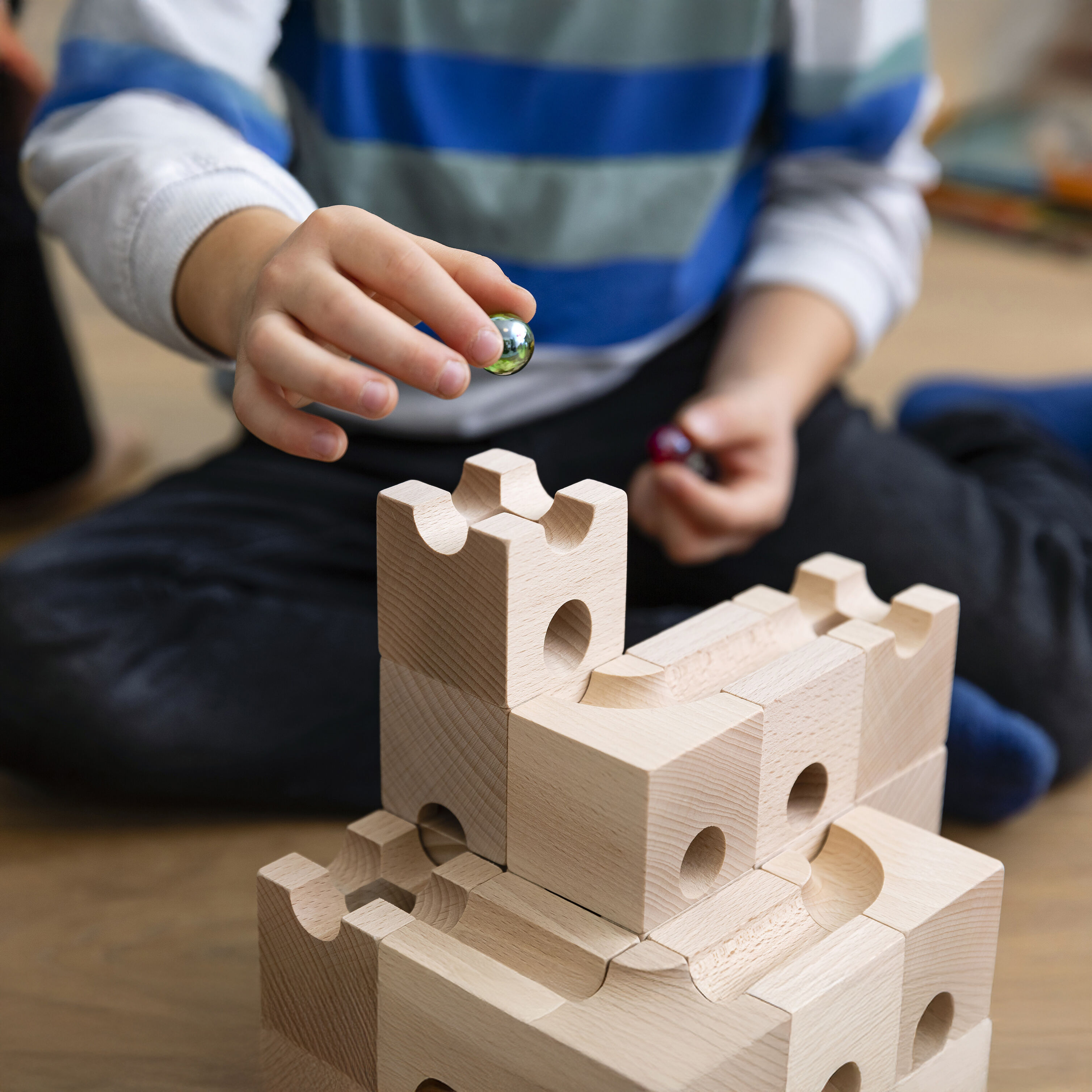 Das Bild zeigt das Cuboro Kugelbahn Starter-Set »STANDARD« mit 32 naturbelassenen Holzelementen und fünf Kugeln. Die sorgfältig gearbeiteten, quaderförmigen Bausteine aus unbehandeltem Schweizer Buchenholz liegen ordentlich arrangiert in einer stabilen Box. Das Set vermittelt einen hochwertigen, nachhaltigen Eindruck.