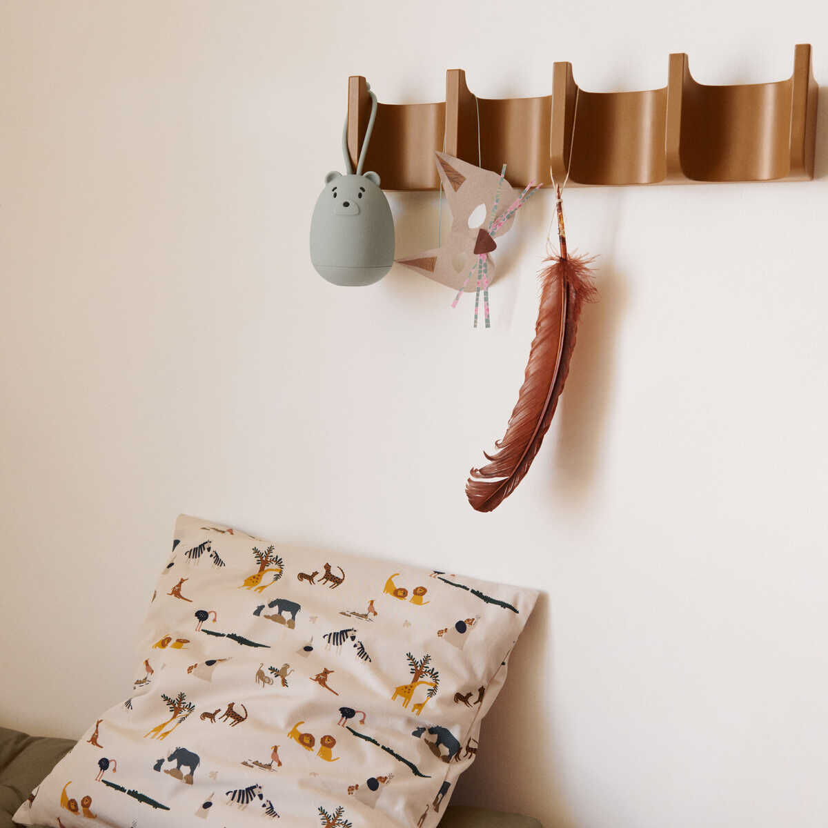 Graues Nachtlicht in Form eines Bären namens Watson hängt an einem braunen Wandregal über einem Bett mit Tiermuster-Bettwäsche. Daneben hängt eine bunte Papierrakete und eine rote Feder.