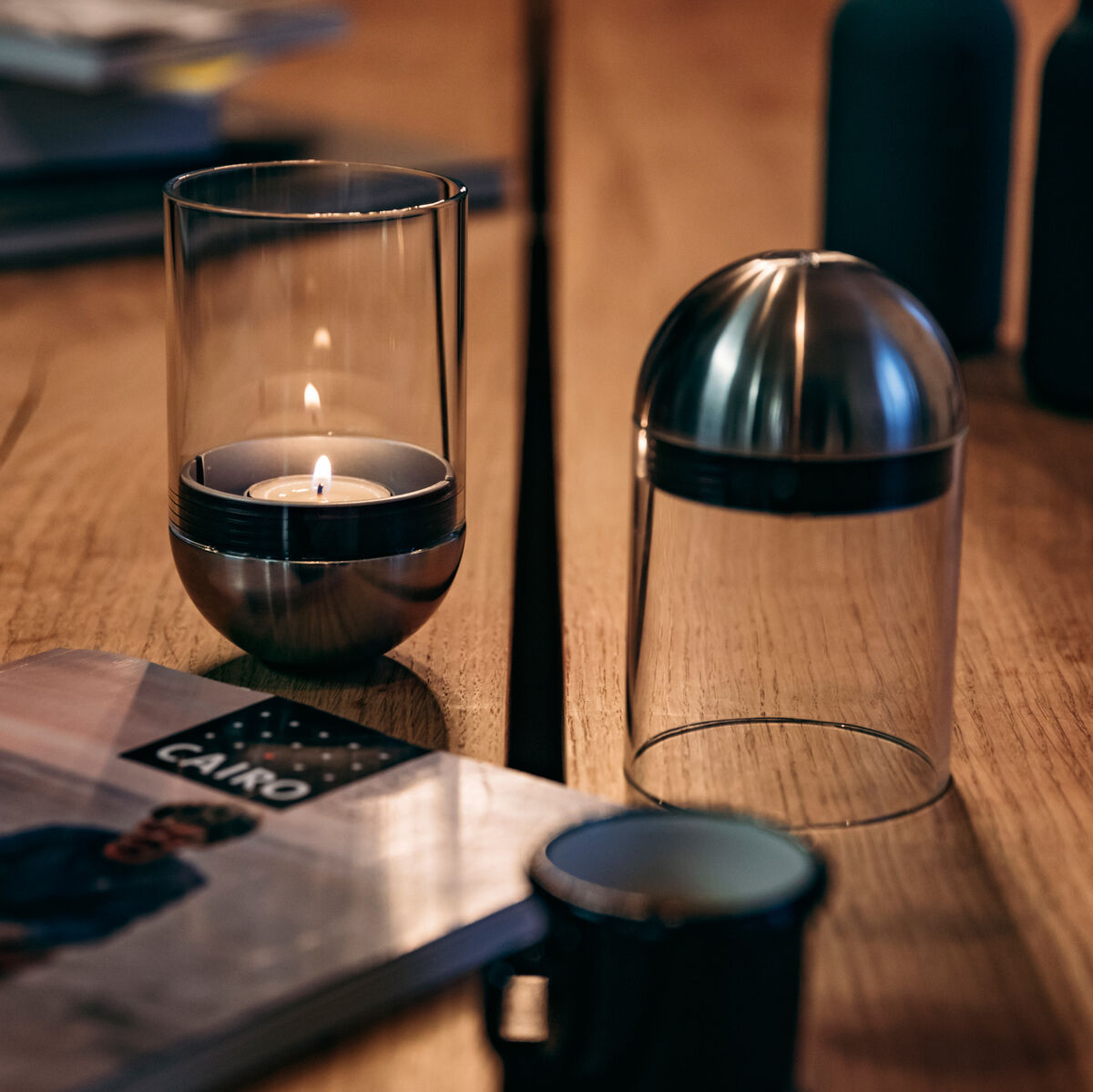 Ein modernes Wohnzimmer mit einer Gravity Candle auf einem Holztisch. Im Hintergrund sind unscharf Bücher, eine Flasche und blaue Dekorationsobjekte zu sehen.