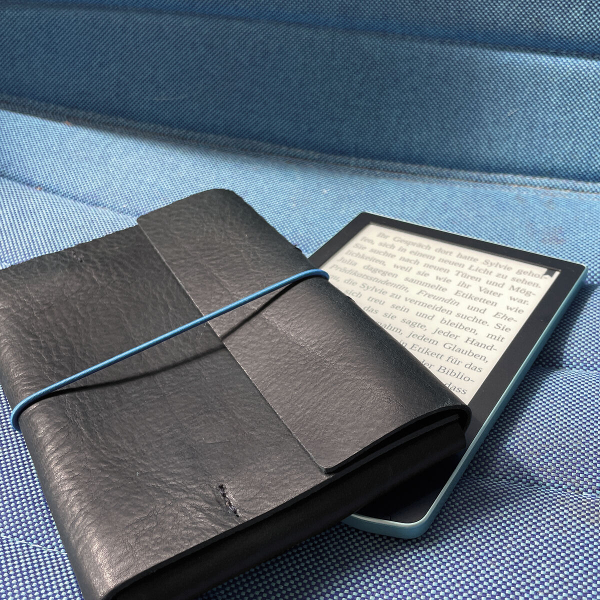 Ein E-Book Reader in einer schwarzen Lederhülle liegend auf einer blauen Oberfläche.