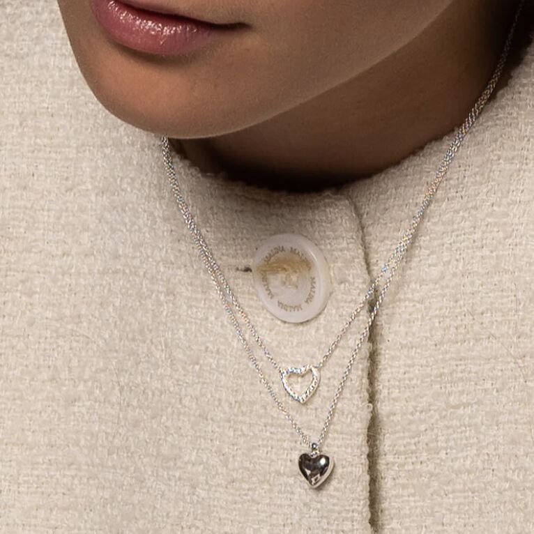 Nahaufnahme einer Frau, die ein doppellagiges Collier mit zwei Herzanhängern aus Silber trägt. Das Schmuckstück liegt auf einem hellen, cremefarbenen Oberteil und ist dezent sowie elegant gestaltet.