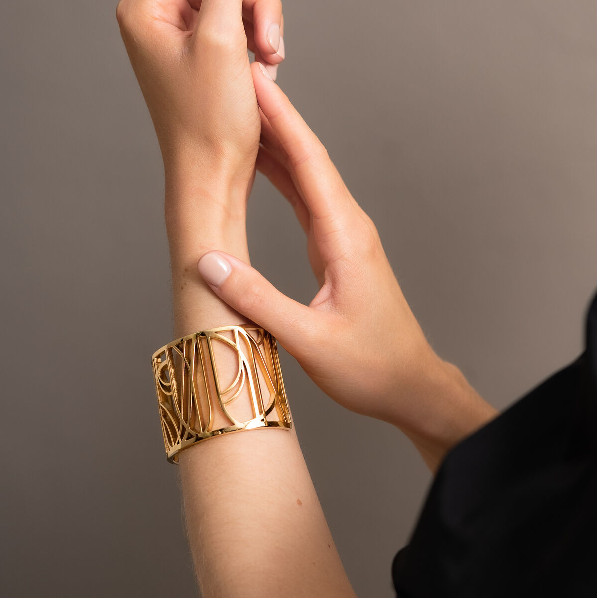 Goldener Armreif »DEW« an einem Handgelenk getragen, elegante und stilvolle Darstellung vor einem beigen Hintergrund.