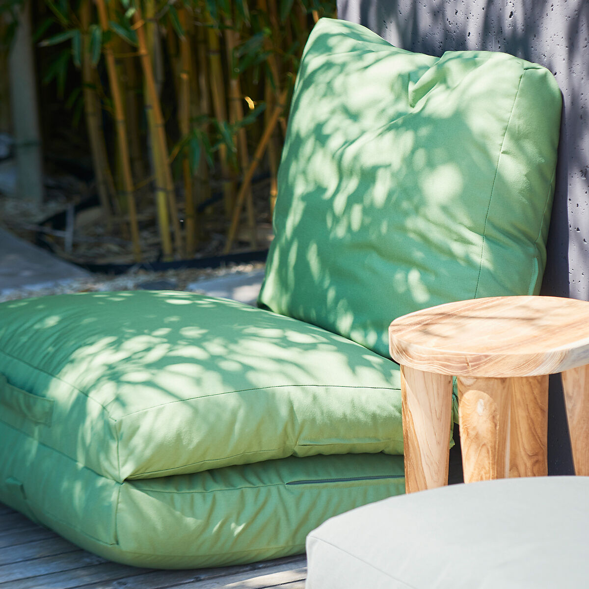 Eine grüne Gartenmatratze »Sheffield« mit Rückenstütze neben einem kleinen Holztisch auf einer Terrasse mit Bambus im Hintergrund.