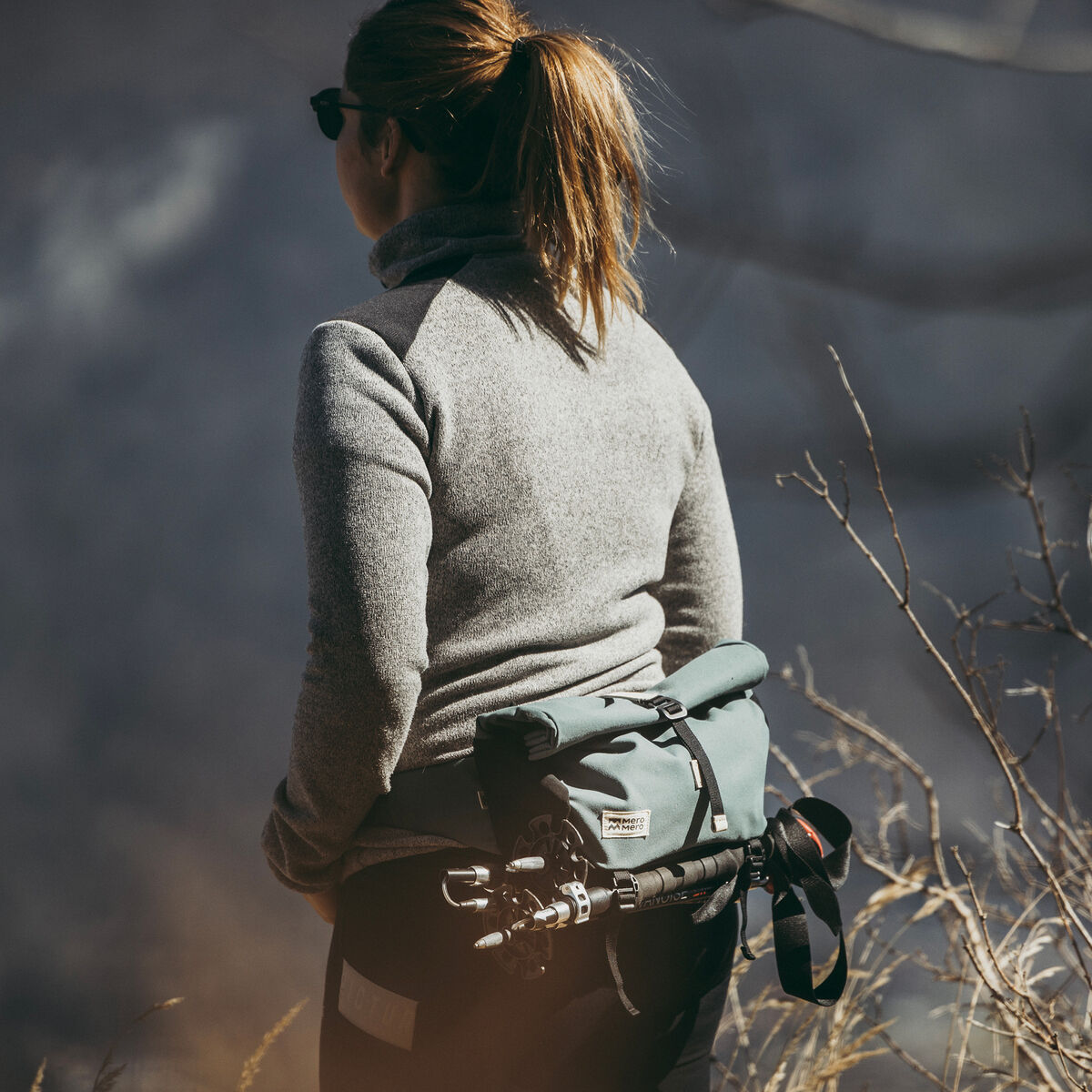 Eine Person im Outdoor-Bereich trägt eine Lenkertasche »Piha« an der Hüfte. Die Tasche ist grau und hat schwarze Details, ideal für Wandern und Fahrradfahren in der Natur.