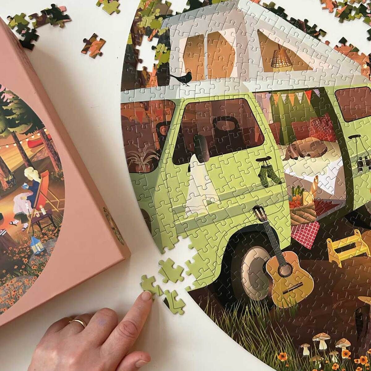 Ein teilweise fertiggestelltes Puzzle mit einem Bild von einem grünen Camper und einer Naturkulisse. Eine Hand fügt ein Puzzleteil hinzu.