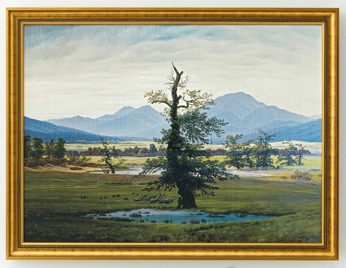 Gerahmtes Gemälde von Caspar David Friedrich mit dem Titel „Der einsame Baum“ aus dem Jahr 1822, das einen markanten, einzeln stehenden Baum inmitten einer grünen Wiesenlandschaft mit Bergen im Hintergrund unter bewölktem Himmel zeigt. Das Bild repräsentiert die romantische Malerei und vermittelt eine ruhige, melancholische Stimmung.