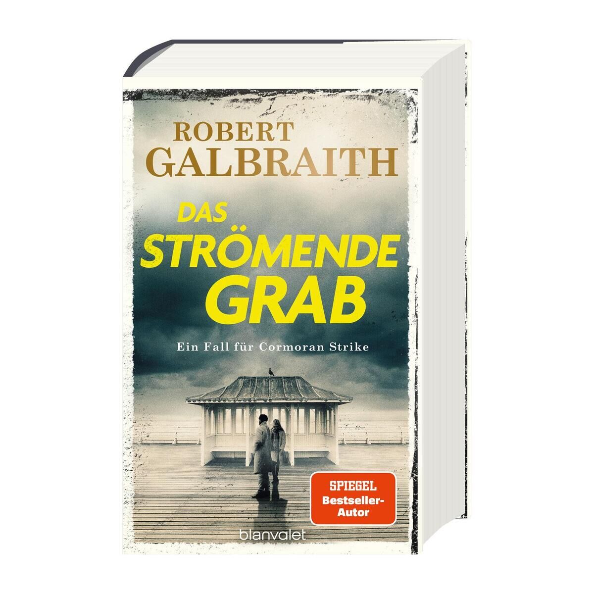 Buchumschlag von 'Das strömende Grab' von Robert Galbraith. Das Cover zeigt einen menschenleeren Pavillon an einem nebligen Strand. Im Vordergrund sind zwei schemenhafte Figuren zu sehen, die auf das Meer blicken. Der Titel des Buches ist in großen gelben Buchstaben geschrieben.