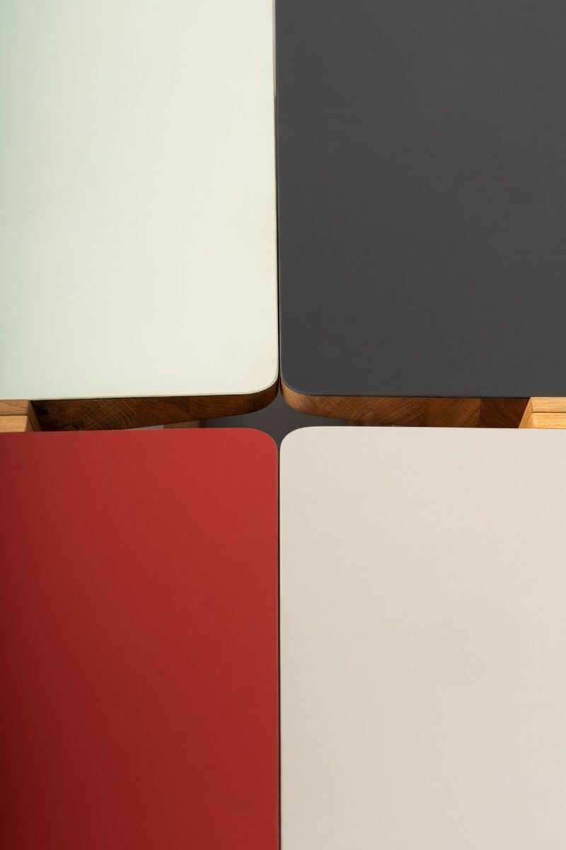 Ein modernes Stehpult mit einer Holzkonstruktion. Es enthält vier farbige Panelen in Weiß, Schwarz, Rot und naturbelassenem Holz und haben eine glatte, matte Oberfläche.