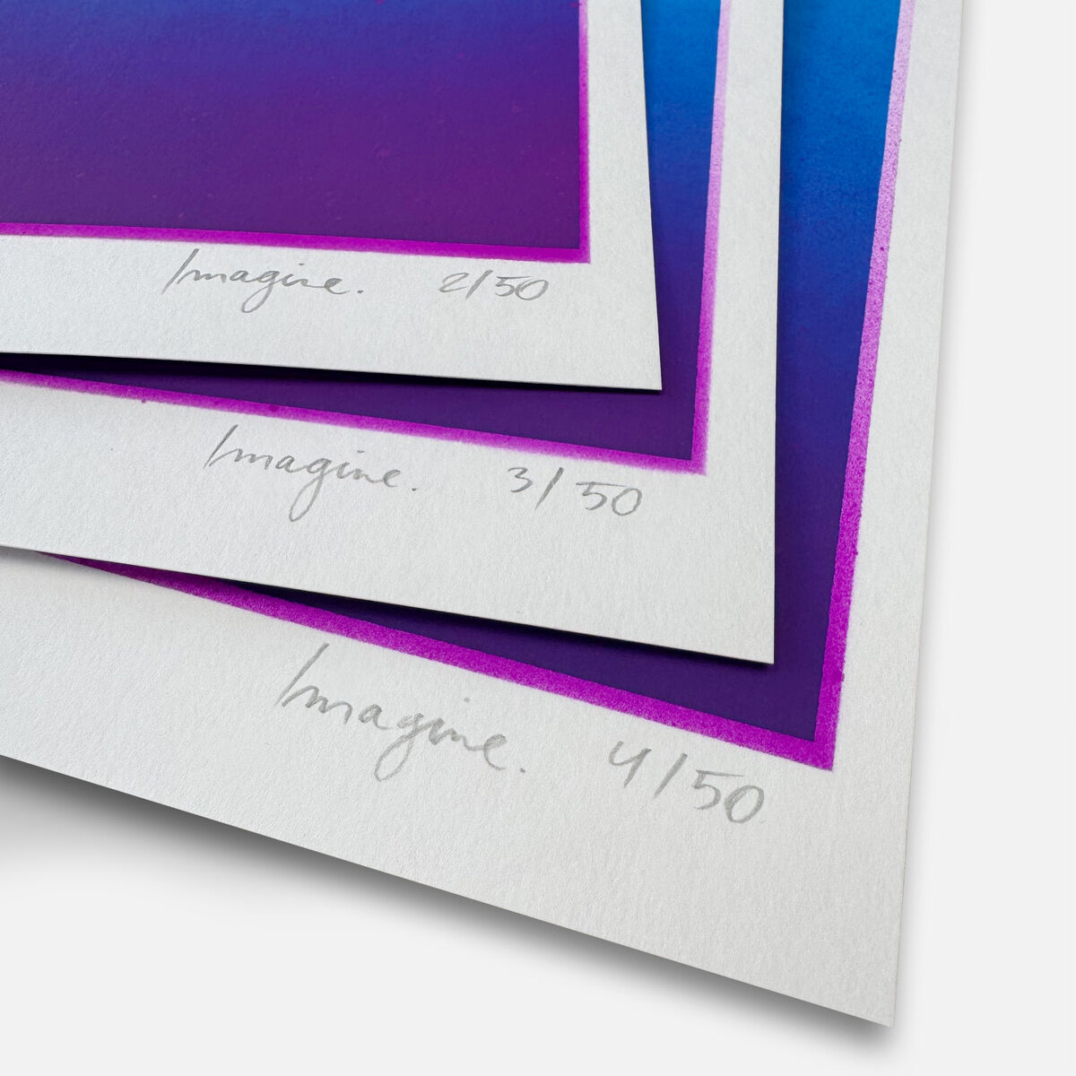 Mehrere nummerierte und vom Künstler Daniel Lisson signierte Originale der ZEIT-Sonderedition »Imagine« liegen leicht versetzt übereinander. Die Werke zeigen intensive Farbverläufe in leuchtendem Blau und Violett mit dezenten Sprühlack-Akzenten. Die Unikate wirken hochwertig und modern.