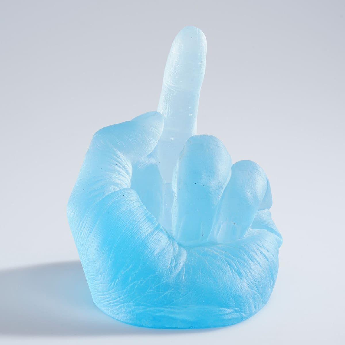 Eine hellblaue Glas-Skulptur von Ai Weiwei mit dem Titel »Study of Perspective in Glass«, die eine Hand zeigt, die den Mittelfinger aufrecht hält. Die Skulptur steht auf einem weißen Hintergrund.