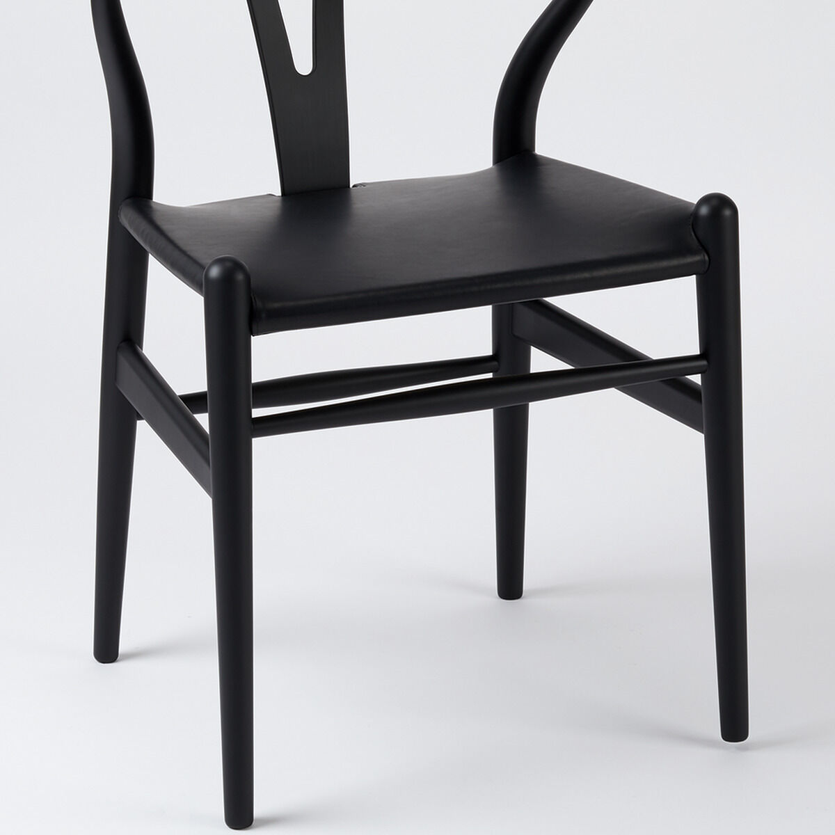 Eine Sonderedition des Wishbone Chair von ZEIT, ein moderner Stuhl aus Buche mit einem Ledersitz, präsentiert in einer minimalistischen schwarzen Ausführung.