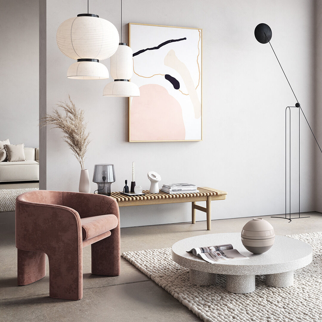 Ein stilvoll eingerichtetes Wohnzimmer mit einem runden, modernen Tisch auf dem ein Geschirr-Set »La Boule« arrangiert ist. Im Hintergrund stehen ein rosa Sessel, ein hölzernes Sideboard mit dekorativen Objekten, eine schlanke Lampe und ein großes, abstraktes Kunstwerk an der Wand. Helle, neutrale Farben dominieren das Bild.