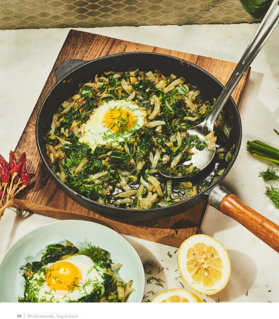 Eine Nahaufnahme eines vegetarischen Gerichts in einer gusseisernen Pfanne, daneben zwei Zitronenhälften und eine Schüssel mit einem Spiegelei und Gemüse, aus dem Kochbuch »Wochenmarkt - Vegetarisch«.