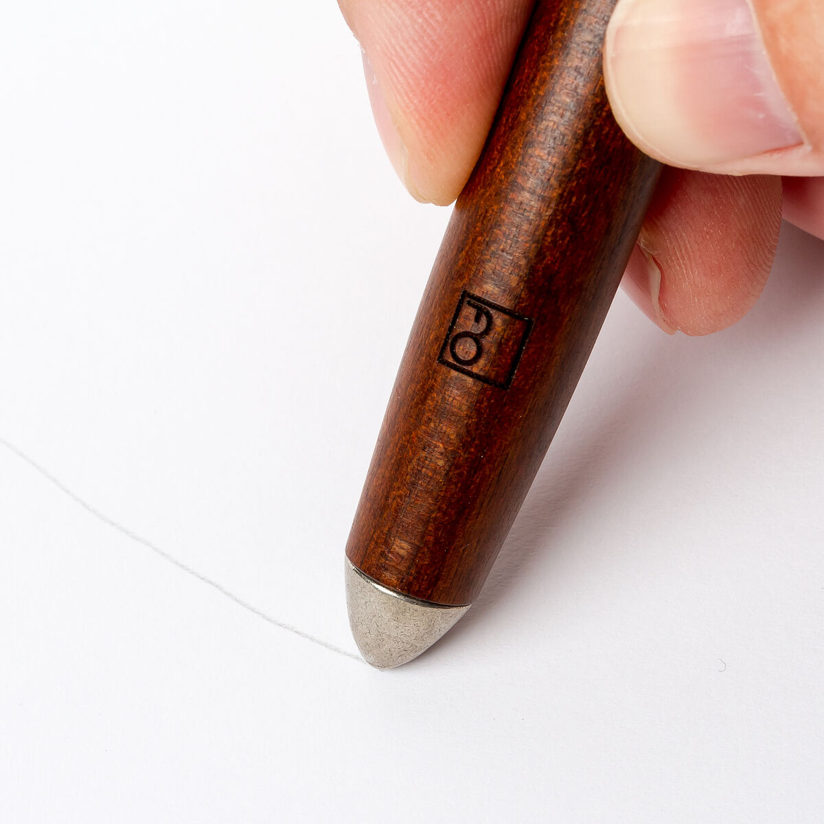 Ein traditioneller Aquarellpinsel mit Ethergraf®-Metallspitze wird auf einem weißen Hintergrund von einer Hand gehalten. Der Pinsel hat einen braunen Holzgriff und eine glänzende Metallspitze.
