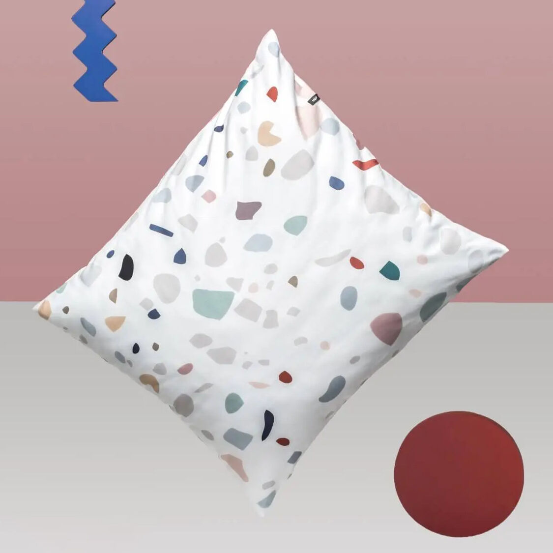 Detailaufnahme eines Kissens aus der Bettwäsche „Terrazzo“ von HOP DESIGN SP Z O O für Morgenstern. Das Kissen zeigt ein weißes Baumwoll-Satin-Gewebe mit unregelmäßigen Farbklecksen in Pastelltönen vor einem stilisierten, modern-minimalistischen Hintergrund.