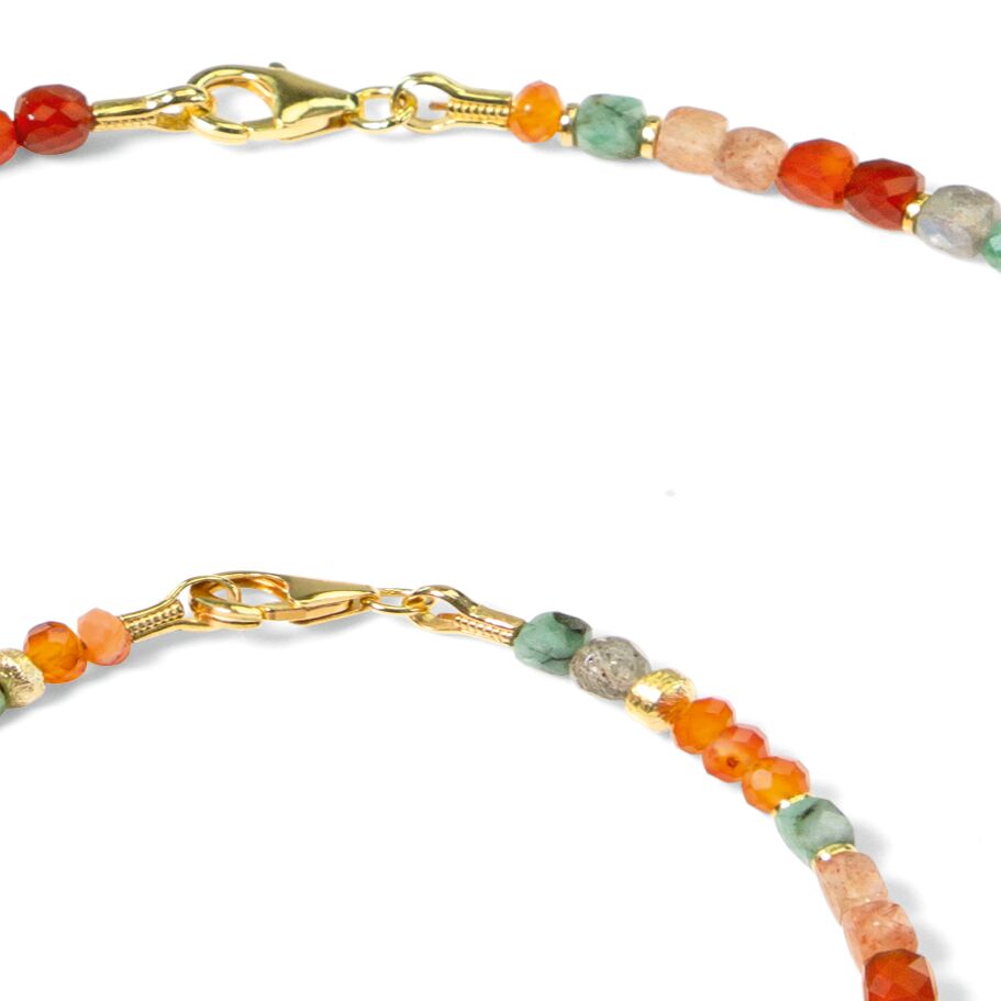 Detailaufnahme eines filigranen Damenarmbands namens "Avril" der Marke Ars mundi. Das Armband besteht aus kleinen, facettierten Edelsteinperlen in den Farben Rot, Orange, Grün und Beige, kombiniert mit vergoldeten Zwischenelementen und einem goldenen Karabinerverschluss.