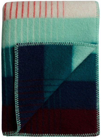 Eine gefaltete, mehrfarbige Lammwolldecke mit einem geometrischen Muster in Blau, Rot, Grün und Creme.