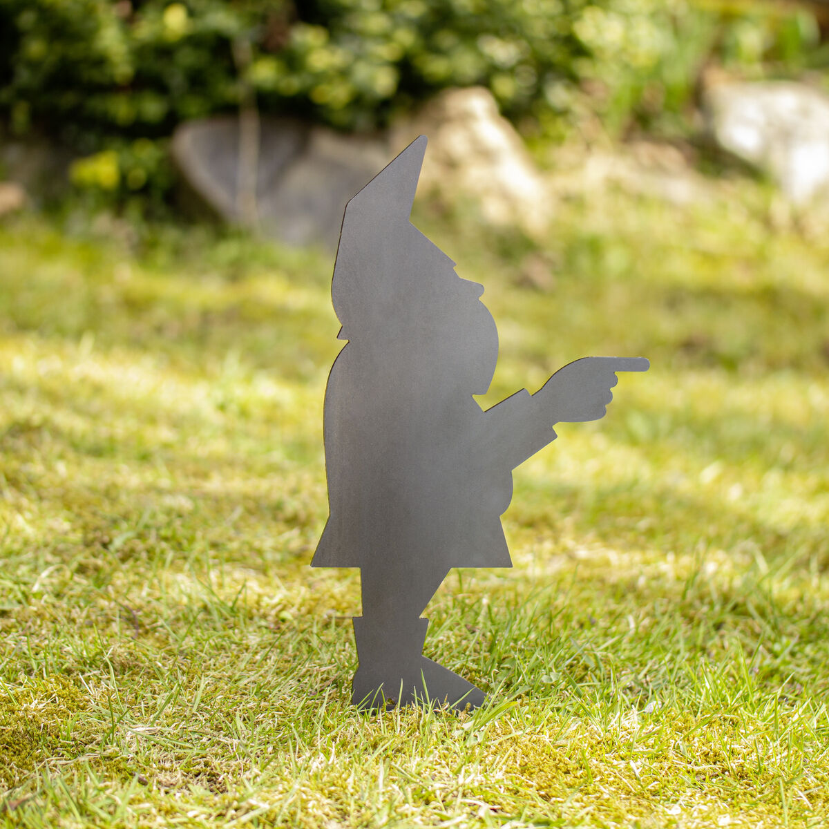Scherenschnitt eines Gartenzwergs aus Metall, der mit dem Finger nach rechts zeigt, auf einer Rasenfläche aufgestellt.
