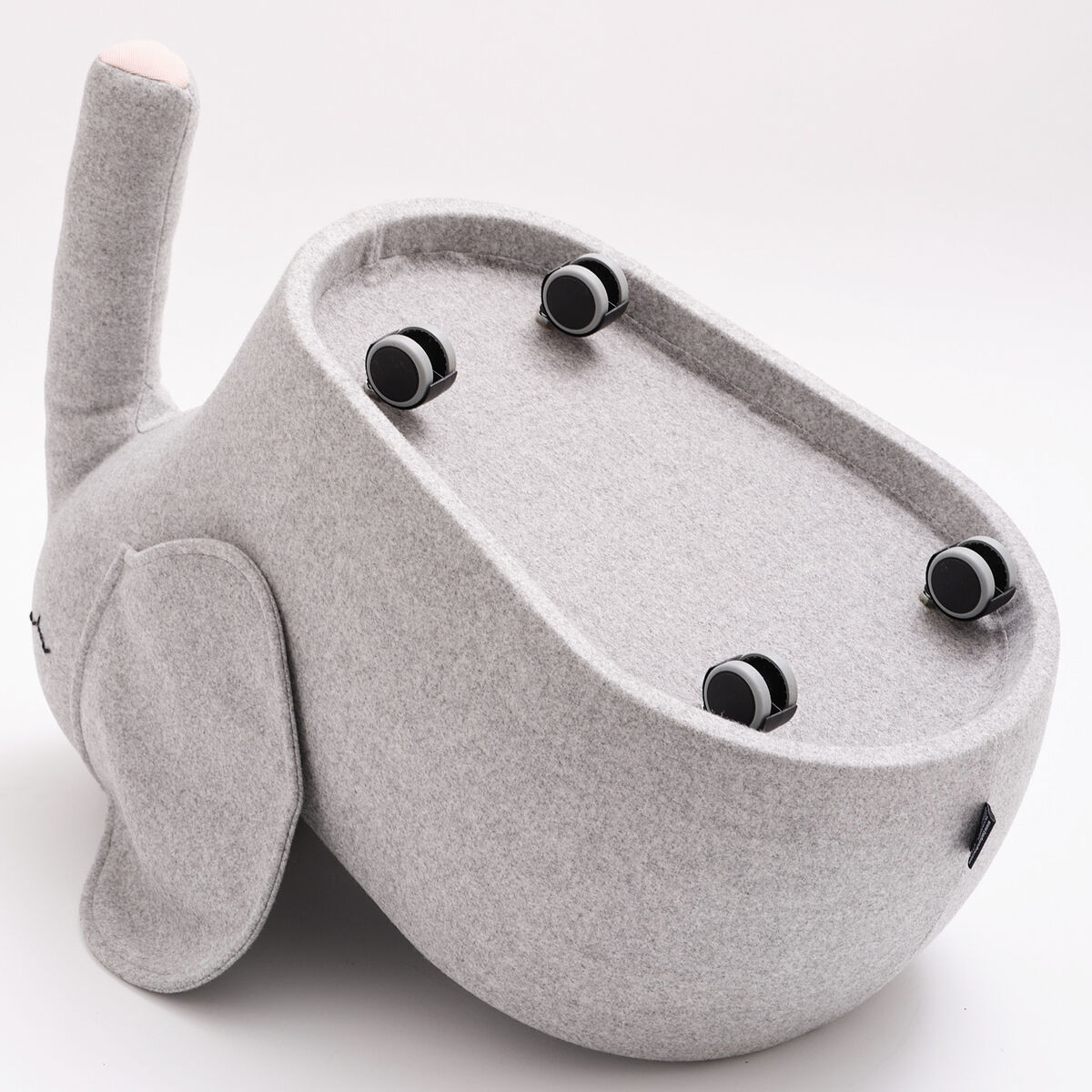 Ein Rollelefant namens »bou« mit einem weichen, grauen Stoffbezug und Holzrollen. Das Produkt, ein Kinderspielzeug und Sitzhocker in Elefantenform, ist auf einem weißen Hintergrund abgebildet.