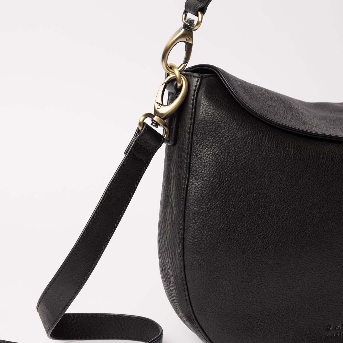 Die Abbildung zeigt eine schwarze Umhängetasche aus Kunstleder mit dezenter Narbung. Die Tasche besitzt einen verstellbaren Schulterriemen mit goldfarbenen Metallelementen. Das schlichte, moderne Design eignet sich für den Alltag oder besondere Anlässe.
