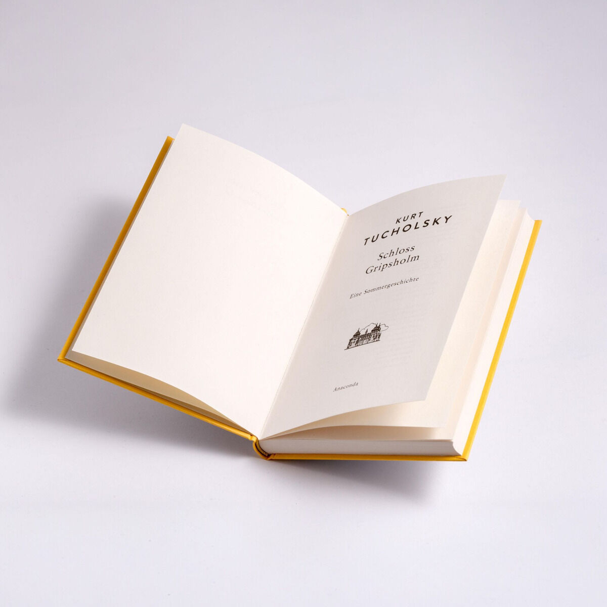 Ein geöffnetes Buch mit dem Titel 'Schloss Gripsholm' von Kurt Tucholsky, präsentiert auf einem weißen Hintergrund. Die Buchseiten sind weiß, und der Buchumschlag hat eine gelbe Außenfläche. Das Titelblatt zeigt den Text sowie eine kleine Illustration eines Schlosses.