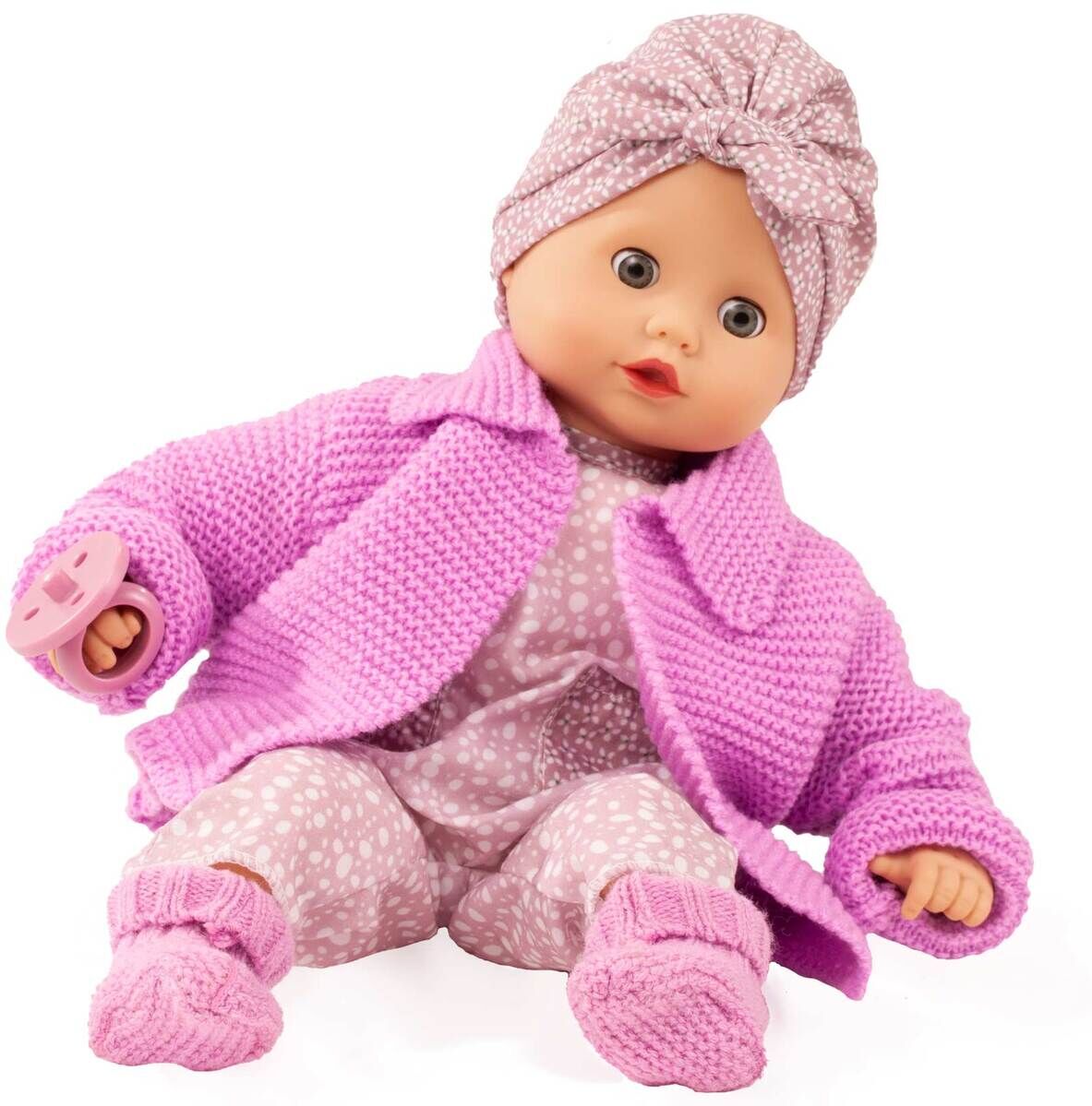 Die Puppe »Muffin Baby Soft Mood« sitzt aufrecht und trägt ein rosa-lilafarbenes Strickjäckchen, ein gemustertes Outfit und eine passende Mütze. In der Hand hält sie einen Schnuller. Die Babypuppe hat ein freundliches Gesicht und ist von weichen Materialien umgeben. Das Foto dient der Produktpräsentation für Kinderspielzeug.