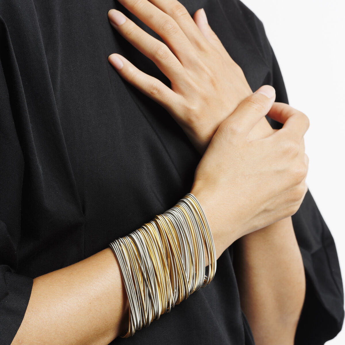Mehrreihiges Armband »Salz und Pfeffer« aus verschiedenen silbernen und goldenen Metallsträngen, getragen am Handgelenk einer Person mit schwarzem, lockerem Oberteil. Das Schmuckstück hebt sich kontrastreich vom Hintergrund ab und wirkt modern sowie elegant.