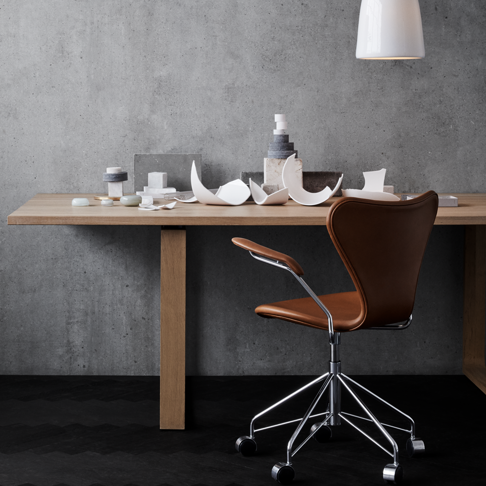 Ein moderner Arbeitsplatz mit einem Holzschreibtisch, auf dem verschiedene weiße Keramiken und Behälter liegen. Ein brauner Drehstuhl steht daneben.