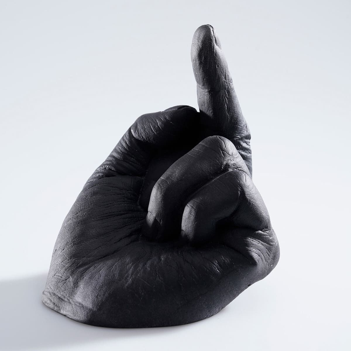 Eine Skulptur von Ai Weiwei mit dem Titel »Study of Perspective in Glass«. Sie zeigt eine schwarze Hand, die einen Finger erhebt. Der Hintergrund der Skulptur ist weiß.