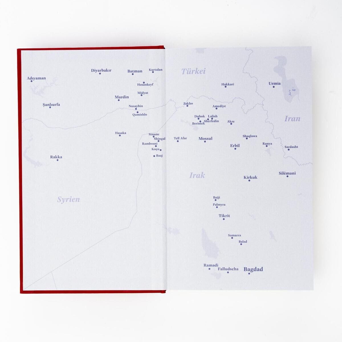 Zweige öffnetes Buch mit rot-weißer Umschlag und einer Karte des Nahen Ostens, mit Fokus auf Länder wie Irak, Syrien, Türkei und Iran.