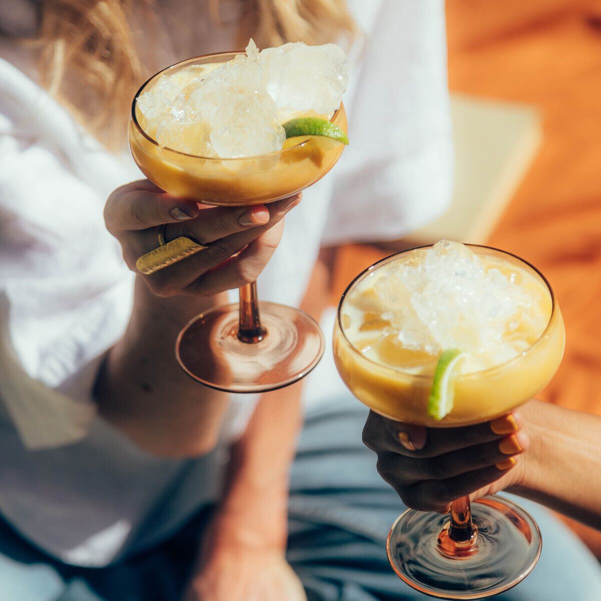 Zwei Personen stoßen im Freien mit Gläsern Eierlikör-Cocktail an, dekoriert mit Limettenscheiben und Crushed Ice. Die Szene wirkt sommerlich und gesellig.