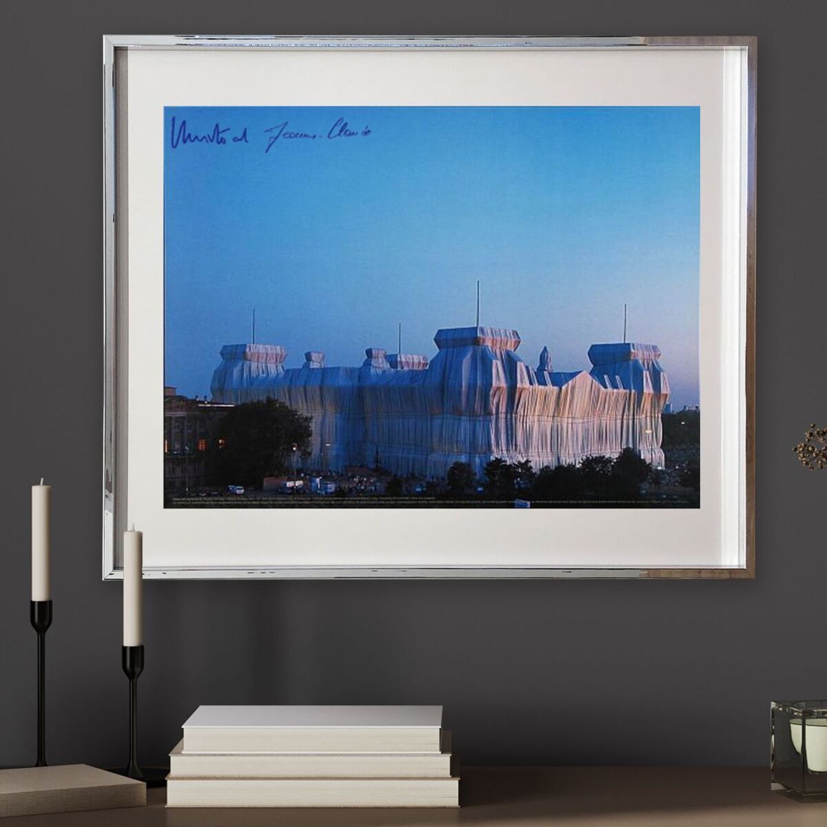 Ein gerahmtes Bild zeigt das verhüllte Reichstagsgebäude in Berlin, ein Kunstprojekt von Christo. Das Bild ist in kühlen Blau- und Weißtönen gehalten. Im Vordergrund befinden sich minimalistische Dekorationselemente.