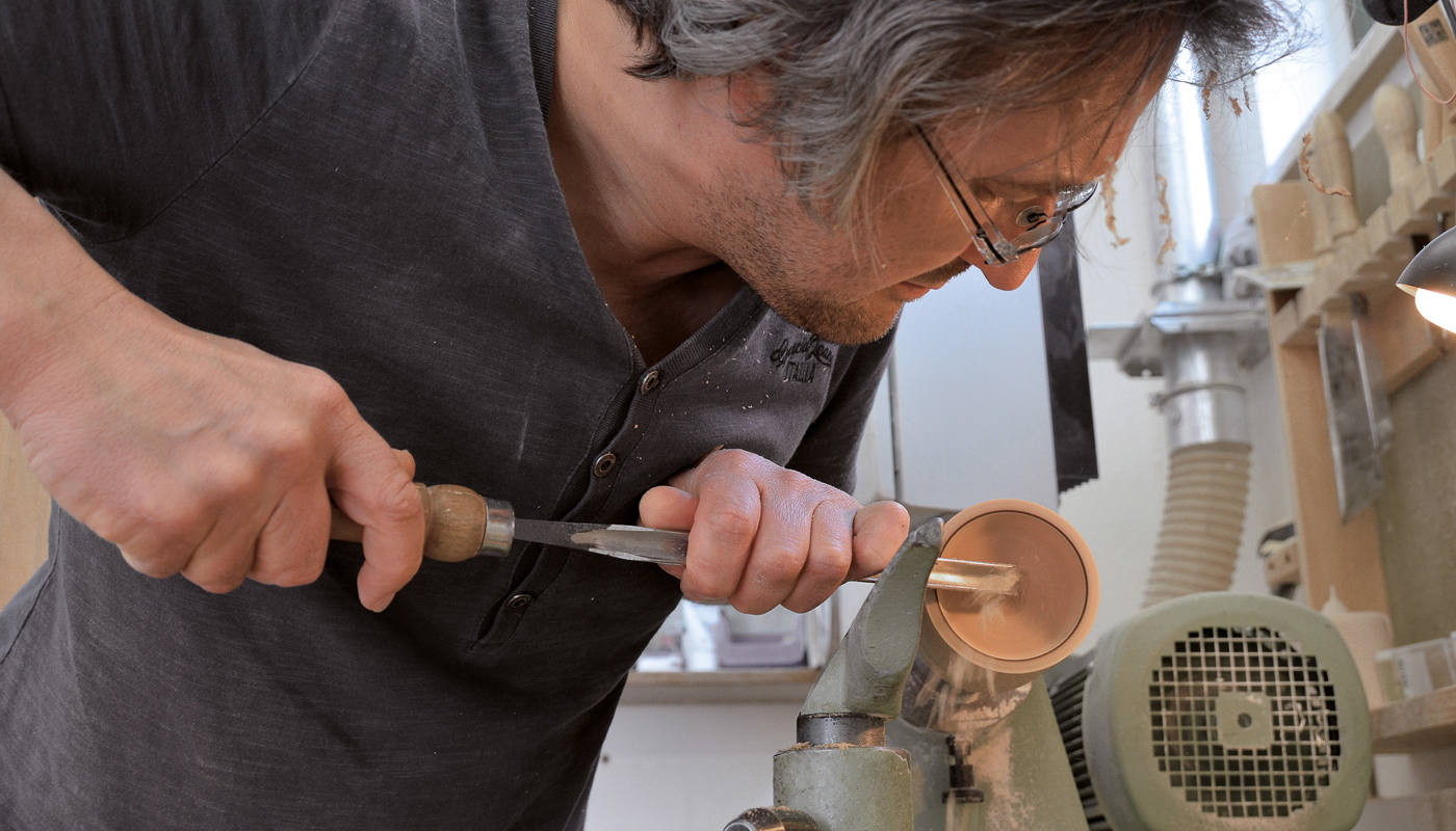 Handwerker bearbeitet Holz mit Drechselbank und Stechbeitel in Werkstatt.