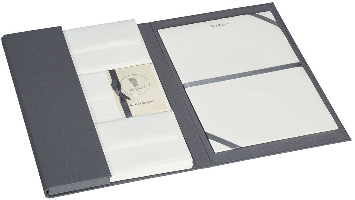 Offene Briefpapiermappe mit edlem Büttenpapier. Die Mappe ist grau und enthält weißes Schreibpapier sowie einige Kuverts. Eine dekorative Schleife hält einen Stapel Papier zusammen.