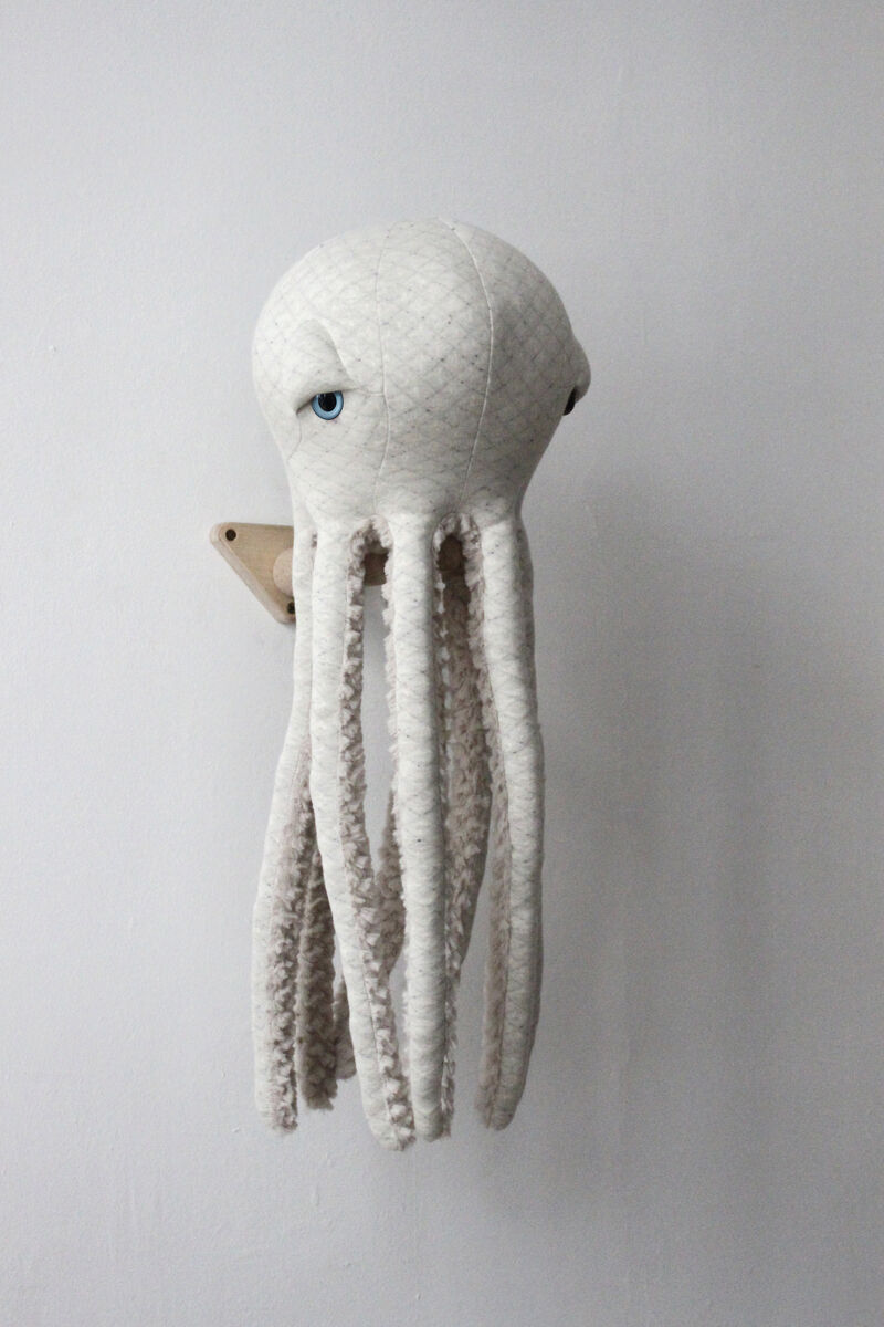 Ein plüschiges, handgefertigtes Spielzeug in Form eines weißen Albino Oktopus mit langen Armen, montiert an einer weißen Wand.