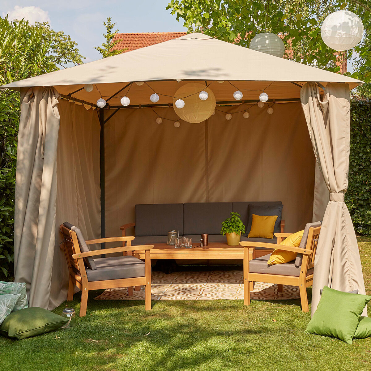 Ein gemütliches Tavira Lounge Set mit vier Teilen, bestehend aus einem überdachten Zelt, zwei Holzbänken mit grauen Polstern, einem Holztisch und dekorativen Kissen in Grün und Gelb, in einem sonnigen Garten arrangiert.